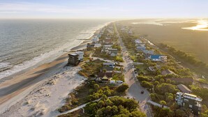 Een kustgebied met woonhuizen langs een strandweg, een zandstrand en een helder uitzicht op de oceaan.