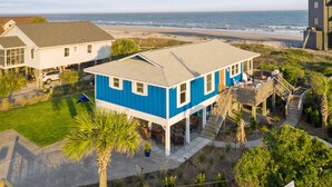 Een huis aan de kust met een blauwe gevel, een overdekte veranda en uitzicht op strand en zee.