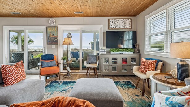 Een ruime woonkamer met houten plafond, grote ramen, een televisie en uitzicht op de omgeving.