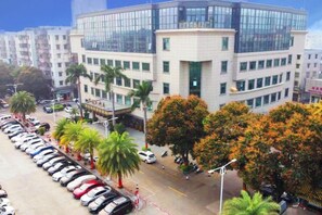 A multi-story building with a modern glass facade, surrounded by parked cars and palm trees. - Garden Hotel (Jiangmen)