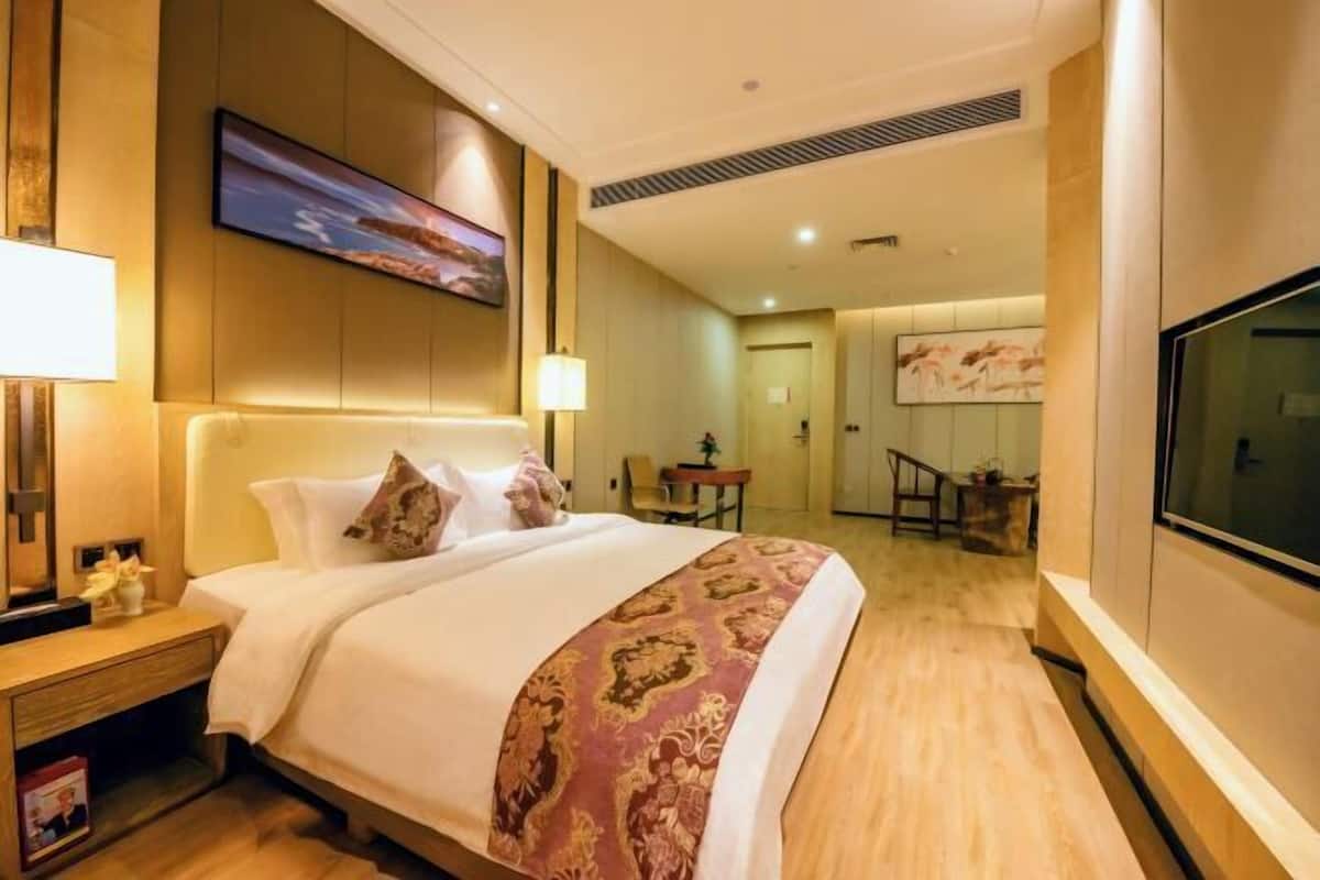 Habitación de hotel con una cama grande, un televisor montado en la pared y un escritorio con una lámpara.