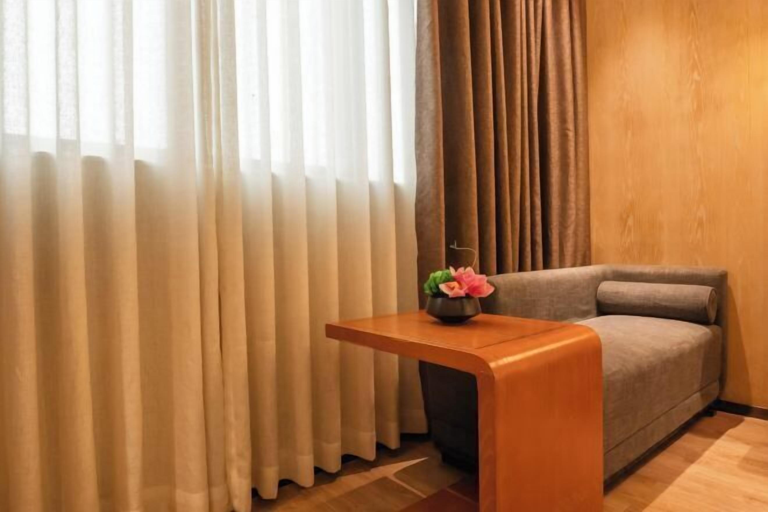 A room with a sofa, a wooden side table, and a vase with flowers.