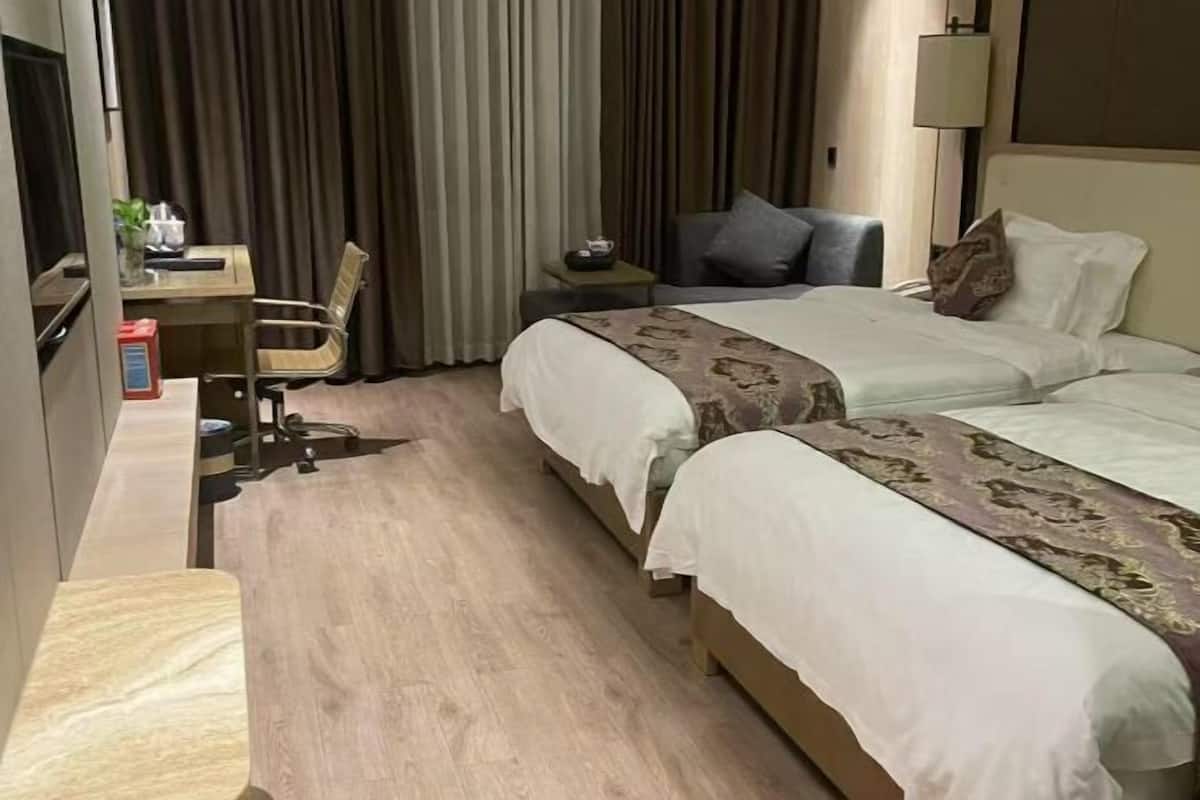 Habitación de hotel con dos camas, un escritorio, una silla, una lámpara y un televisor.