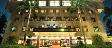 Un hotel con un'ampia entrata, palme e finestre illuminate.