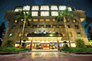 A hotel with a large entrance, palm trees, and illuminated windows. - Garden Hotel (Jiangmen)