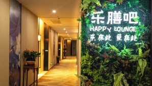A hallway with a sign for Happy Lounge, a potted plant, and a wall decorated with green foliage. - Garden Hotel (Jiangmen)