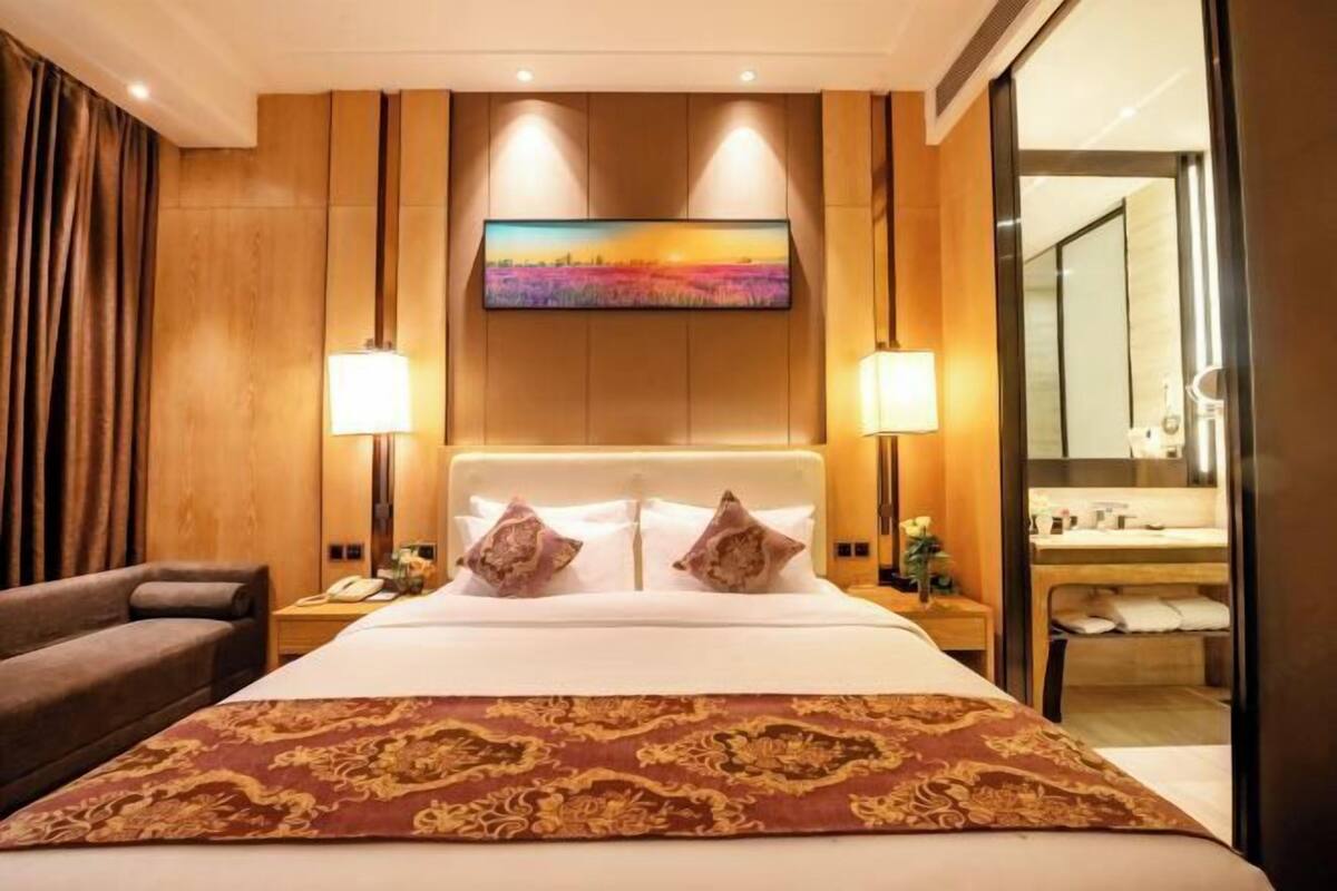 Habitación de hotel con una cama grande, dos lámparas de noche, un televisor de pantalla plana en la pared, un cabecero de madera y un espejo amplio.