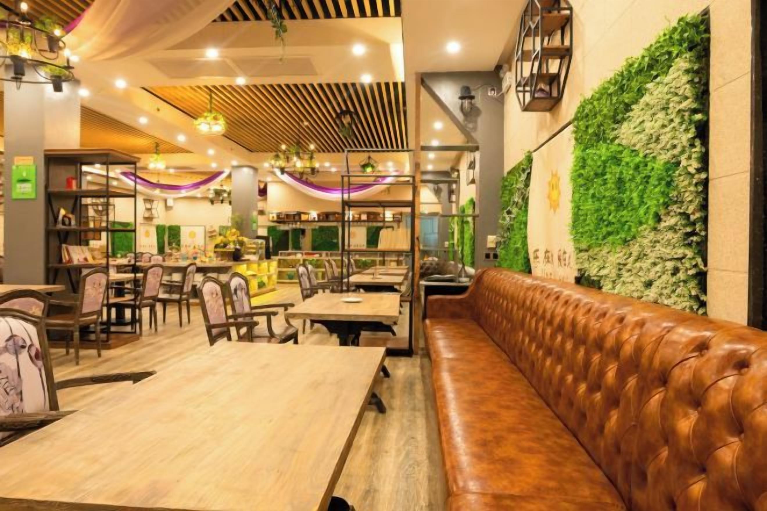 L’intérieur d’un restaurant avec des tables en bois, un coin salon en cuir et un mur vert.
