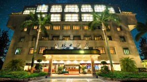 A hotel with a large entrance, multiple floors, and palm trees in front. - Garden Hotel (Jiangmen)