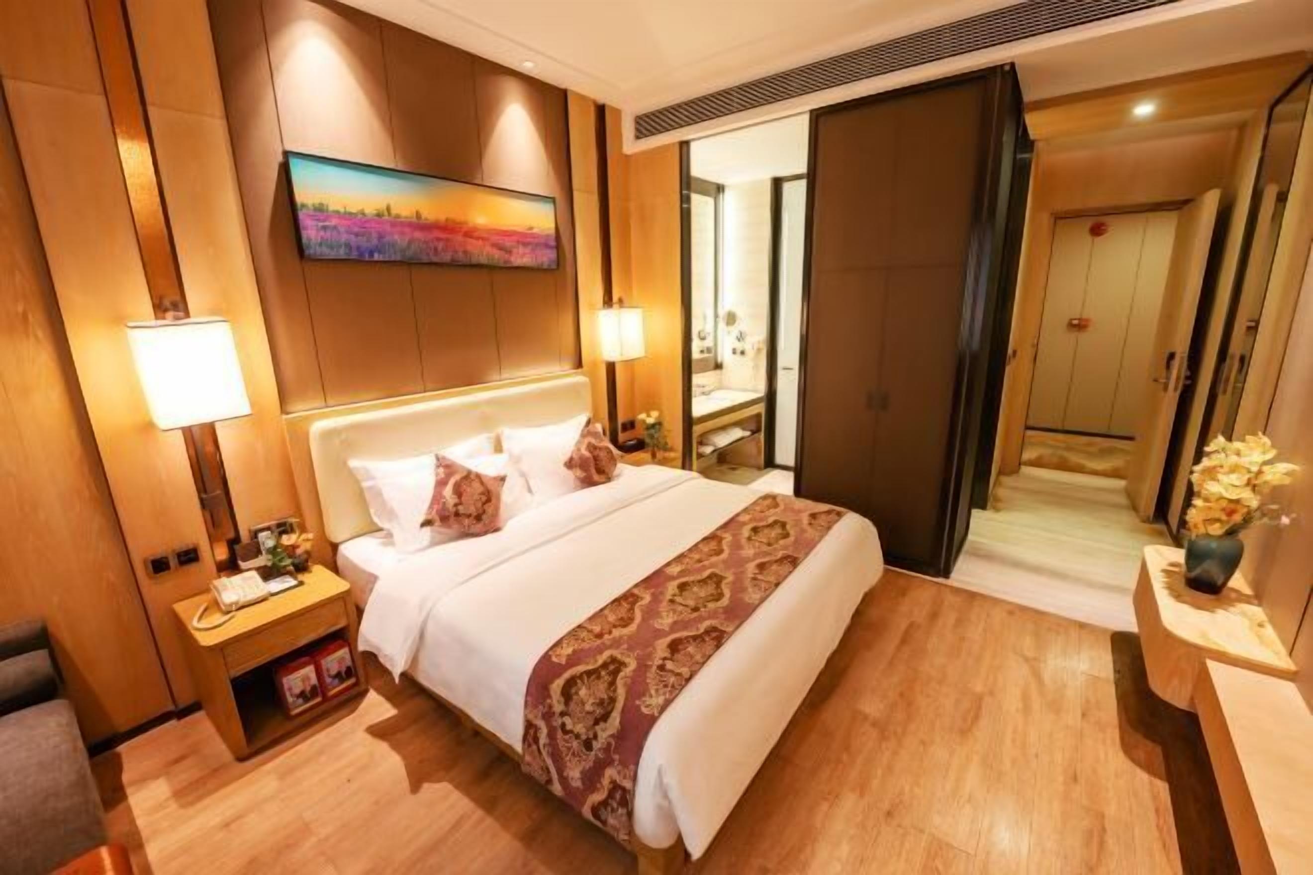 A hotel room with a large bed, a bedside table, a nightstand, a wall-mounted TV, and a mirror.