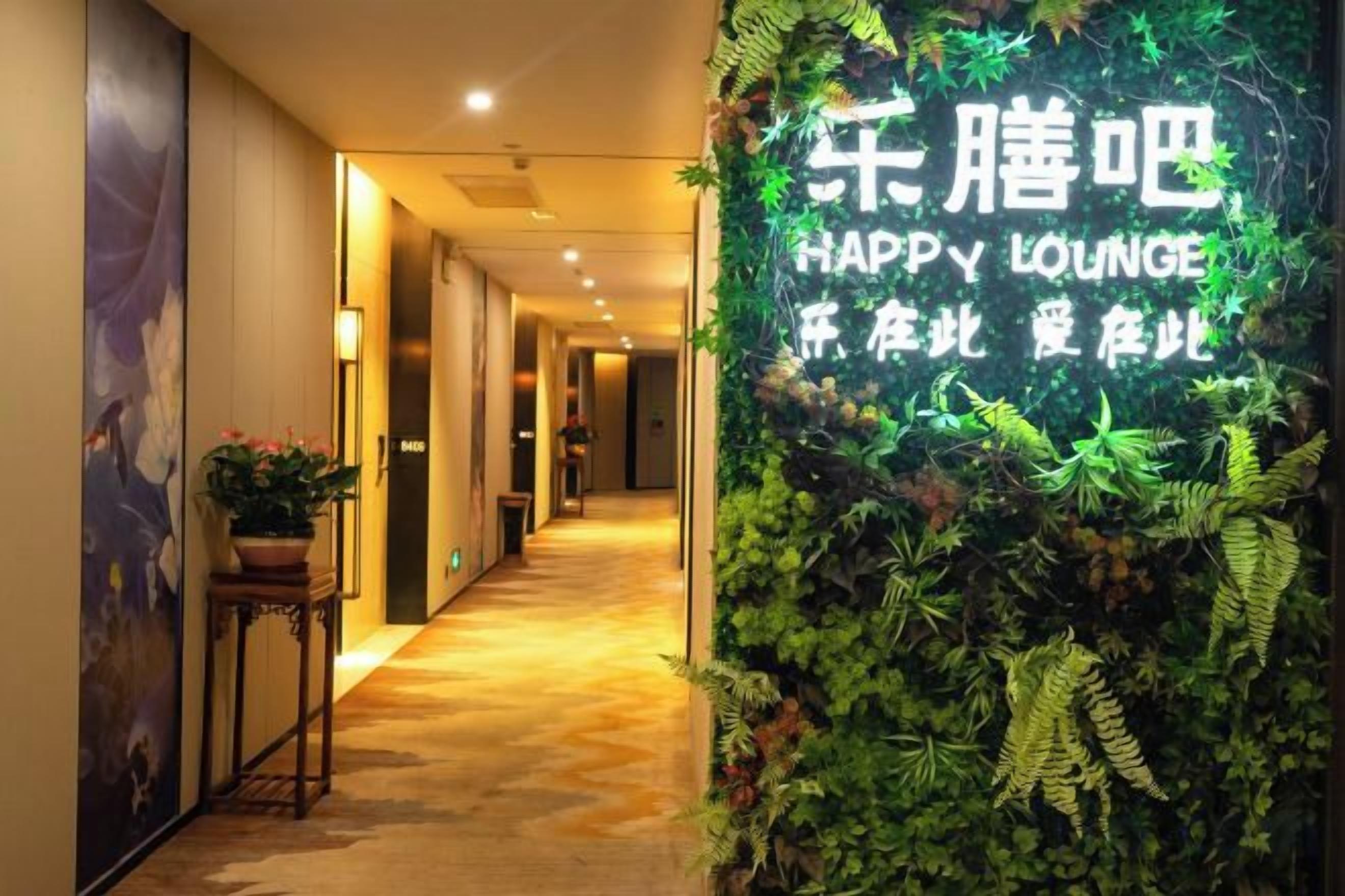 A hallway with a green wall featuring a sign that reads 'HAPPY LOUNGE' and a potted plant on the left.