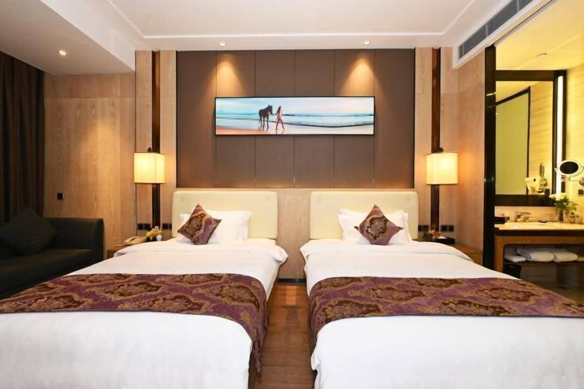 Habitación de hotel con dos camas, un televisor grande montado en la pared y un panel de pared de madera.