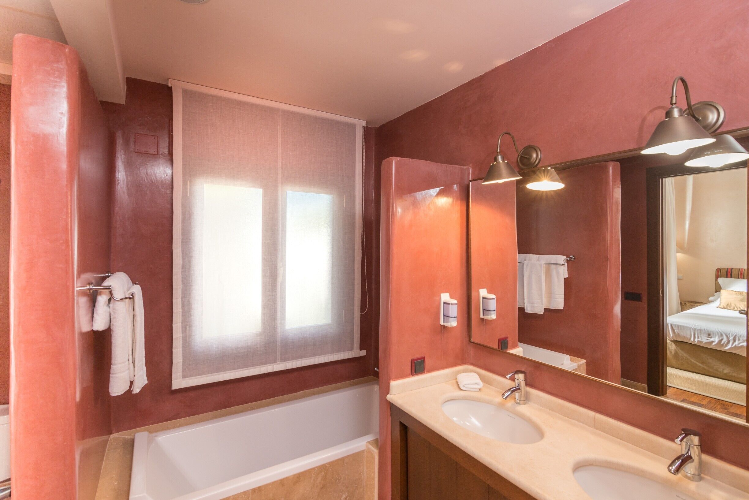 A bathroom with a bathtub, two sinks, a large mirror, and a window with sheer curtains.