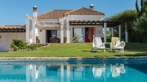 Una casa con piscina, sillas de descanso blancas y un patio cubierto.