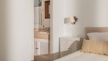 Ein Schlafzimmer mit Bett, Nachttisch, Wandlampe, Badezimmer mit Waschbecken und Spiegel sowie Thermostat an der Wand.