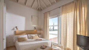 Ein Schlafzimmer mit einem Bett, Nachttischlampen, einem Fernseher und einem Fenster mit Vorhängen.