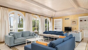 A spacious living room with a high ceiling, large windows, and a TV. - Villa Rosa with Pool, Garden and Wi-Fi (Benalup-Casas Viejas)