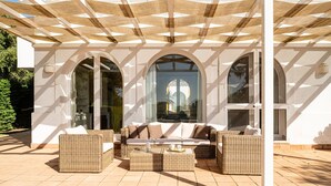 A covered outdoor seating area with wicker furniture and large windows. - Villa Rosa with Pool, Garden and Wi-Fi (Benalup-Casas Viejas)