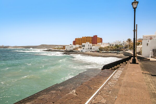 A coastal walkway with a stone pavement, a lamp post, and buildings in the background.