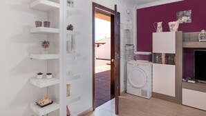 A modern bathroom with a washing machine, shelves with decorative items, and a purple accent wall. - Apartment Apartamento Porís close to the Beach with Shared Pool & Wi-Fi (Arico)
