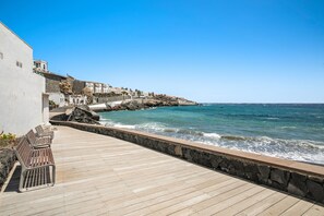 A wooden deck with benches overlooking a rocky coastline and a clear blue sky.