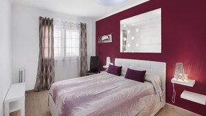 A bedroom with a bed, a white nightstand, a chair, a mirror with lights, and a window with curtains. - Apartment Apartamento Porís close to the Beach with Shared Pool & Wi-Fi (Arico)