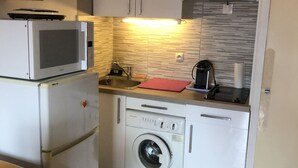 A compact kitchen with a microwave, washing machine, and a small countertop with a kettle. - T2 mezzanine near beach and shops (Saint-Cyprien)