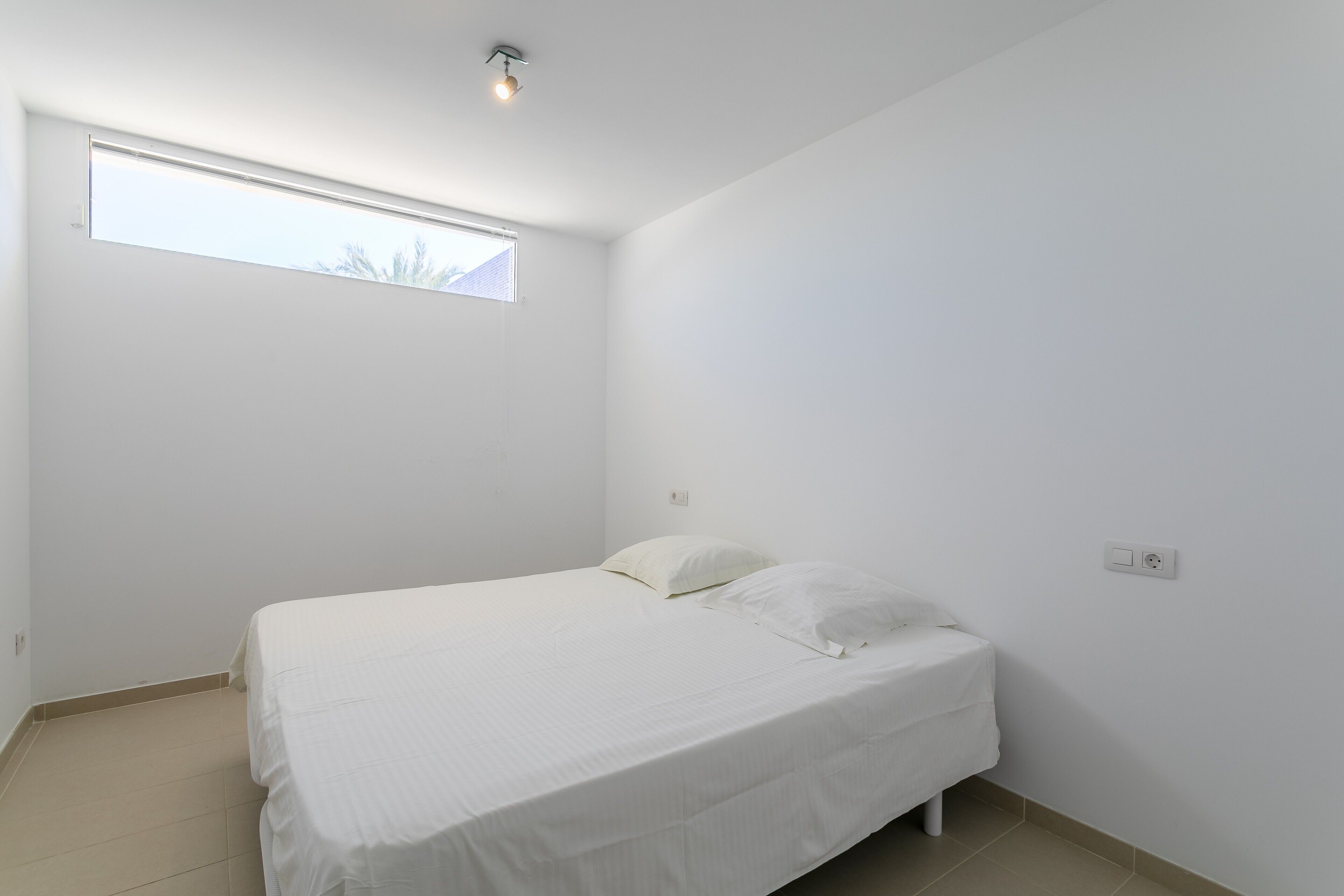 A single bed with white bedding in a room with white walls and a window.