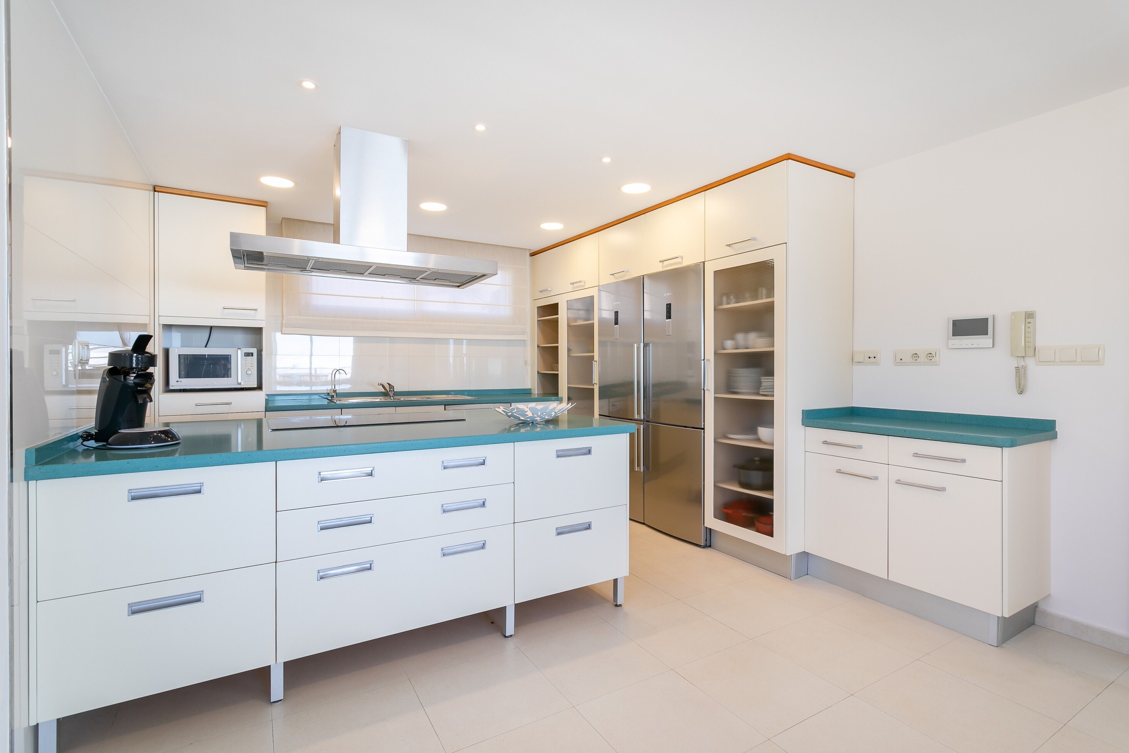 Una cocina moderna con armarios blancos, una encimera azul y un refrigerador de acero inoxidable.