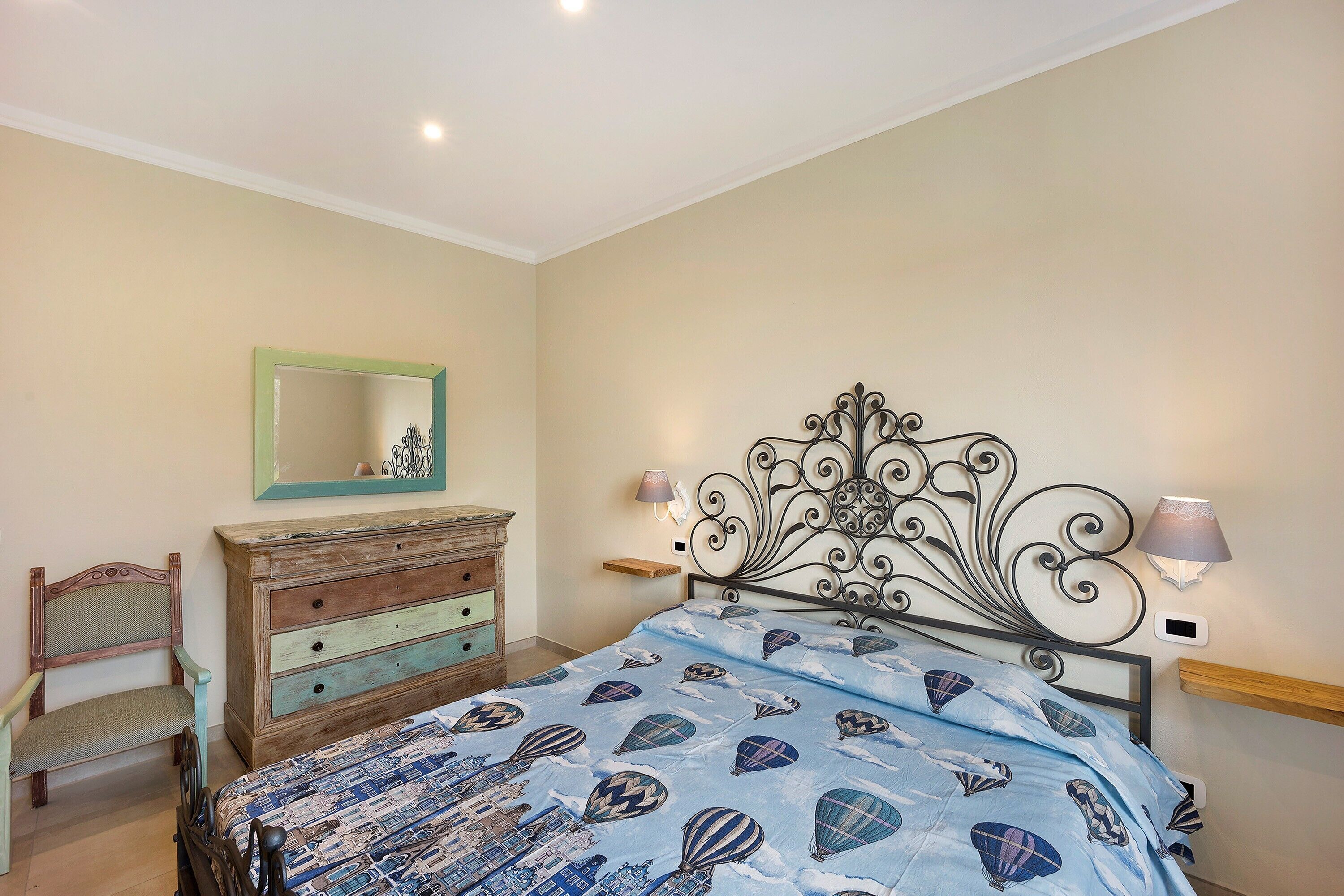 A bedroom with a bed, dresser, chair, and wall-mounted lamp.