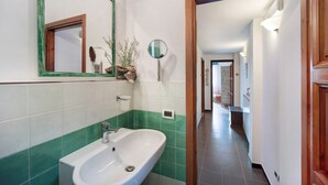 Une salle de bain avec un lavabo blanc, des carreaux verts, un miroir et une porte donnant sur un couloir.