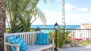 A wooden bench with blue cushions, a palm tree, a lamp post, and a view of the sea.