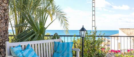 A wooden bench with blue cushions, a palm tree, a lamp post, and a view of the sea.