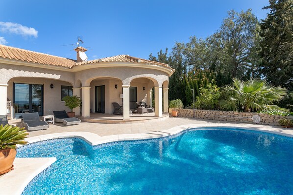 Ein Poolbereich mit einem gewundenen Pool, Sitzgelegenheiten im Freien und einer überdachten Terrasse.