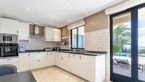 A modern kitchen with white cabinets, a black countertop, and a view of the pool outside.