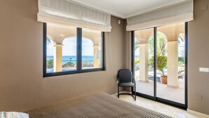 A hotel room with a bed, a chair, large windows, and a view of the sea.