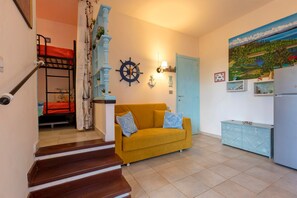 Una sala de estar con una escalera, un sofá amarillo, un reloj de pared, una puerta y un cuadro.