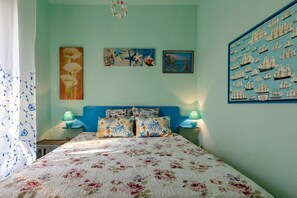 Un dormitorio con cubrecama floral, cabecera azul y decoración náutica en las paredes.