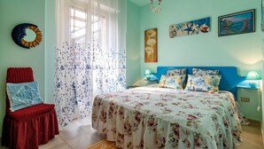 Une chambre à coucher comprenant un lit, une chaise, une table de chevet, une lampe et un mur décoré de tableaux.