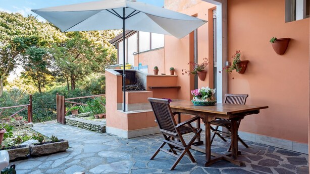 Une terrasse extérieure avec une table et des chaises, un grand parasol et des plantes en pot.