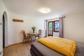Una habitación con cama, una mesa, dos sillas, un jarrón con flores y una ventana con cortinas.