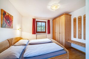 Un dormitorio con dos camas, un armario de madera, un radiador y una ventana con cortinas rojas.
