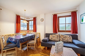 Una habitación con una mesa de comedor, sillas, un sofá, una ventana con cortinas y un reloj en la pared.