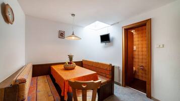 Una habitación compacta con una mesa de comedor, asientos tipo banco, un televisor y una puerta que da a un baño.