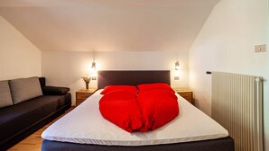 A bedroom with a bed, a nightstand, a lamp, a radiator, and a sofa.