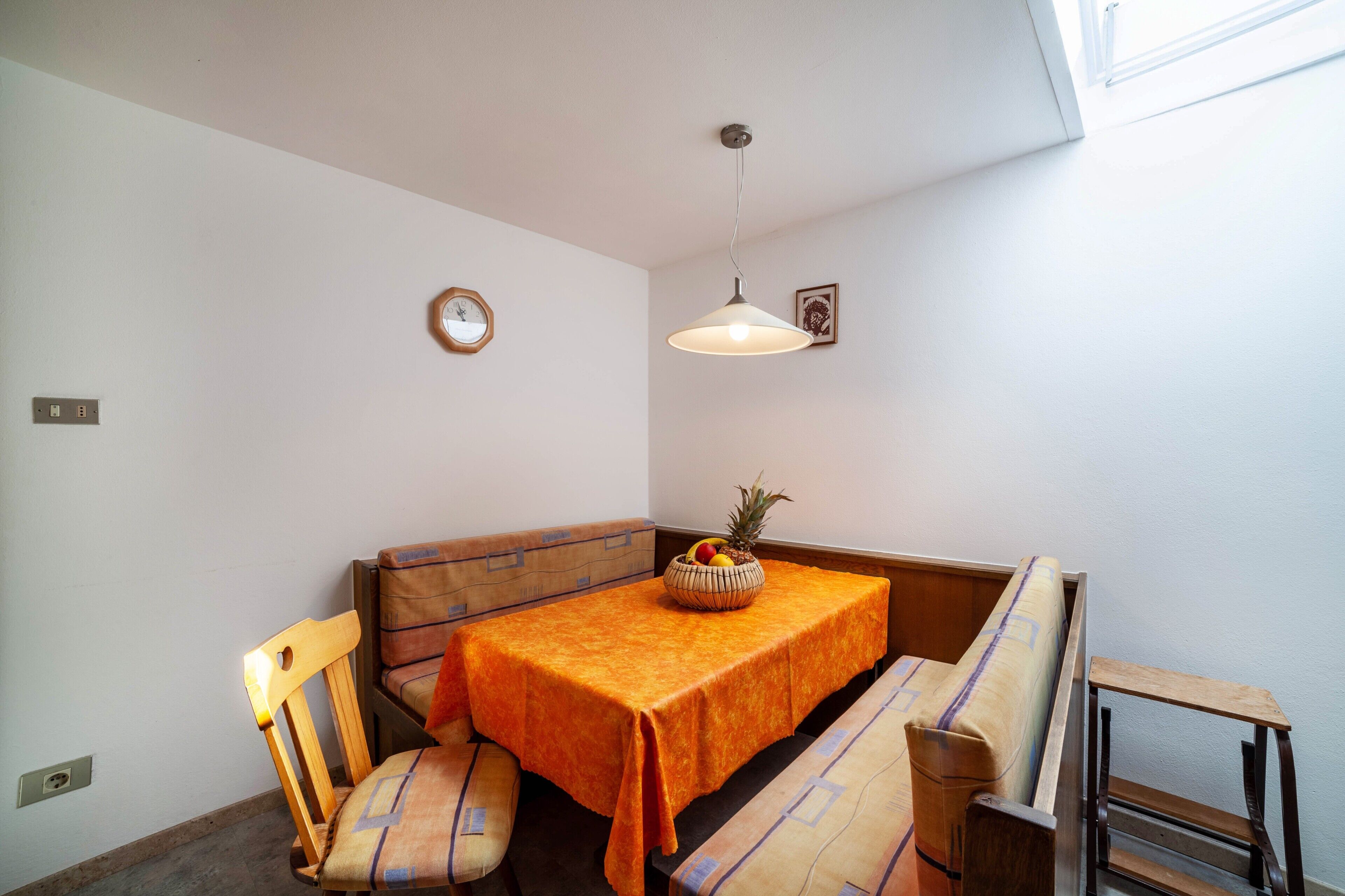 A corner dining area with a table, chairs, a bench, a wall clock, and a hanging light fixture.