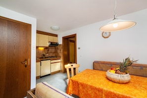 A compact kitchen with wooden cabinets, a dining table with an orange tablecloth, and a fruit bowl on the table.