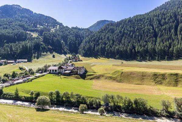 A rural landscape with a large house surrounded by fields, a river, and forested hills.
