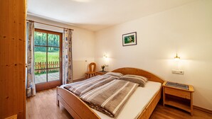 A bedroom with a wooden bed, a nightstand, a desk, a chair, and a window with curtains. - Apartment 'Rieglhof Geiernest' with Mountain View, Garden & Wi-Fi (Graun im Vinschgau)