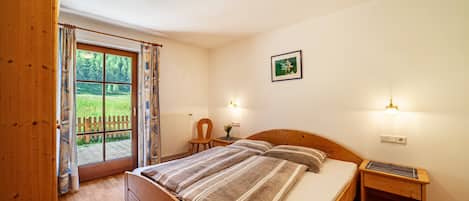 Une chambre à coucher avec un lit en bois, une table de chevet, un bureau, une chaise et une fenêtre avec des rideaux.